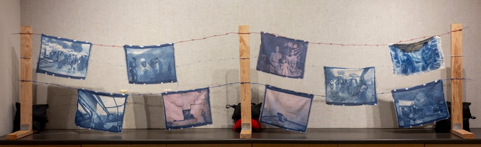 Sueño Americano — cyanotype textiles strung on three rows of red, white, and blue barbed wire, held between three 2x4 fence stands