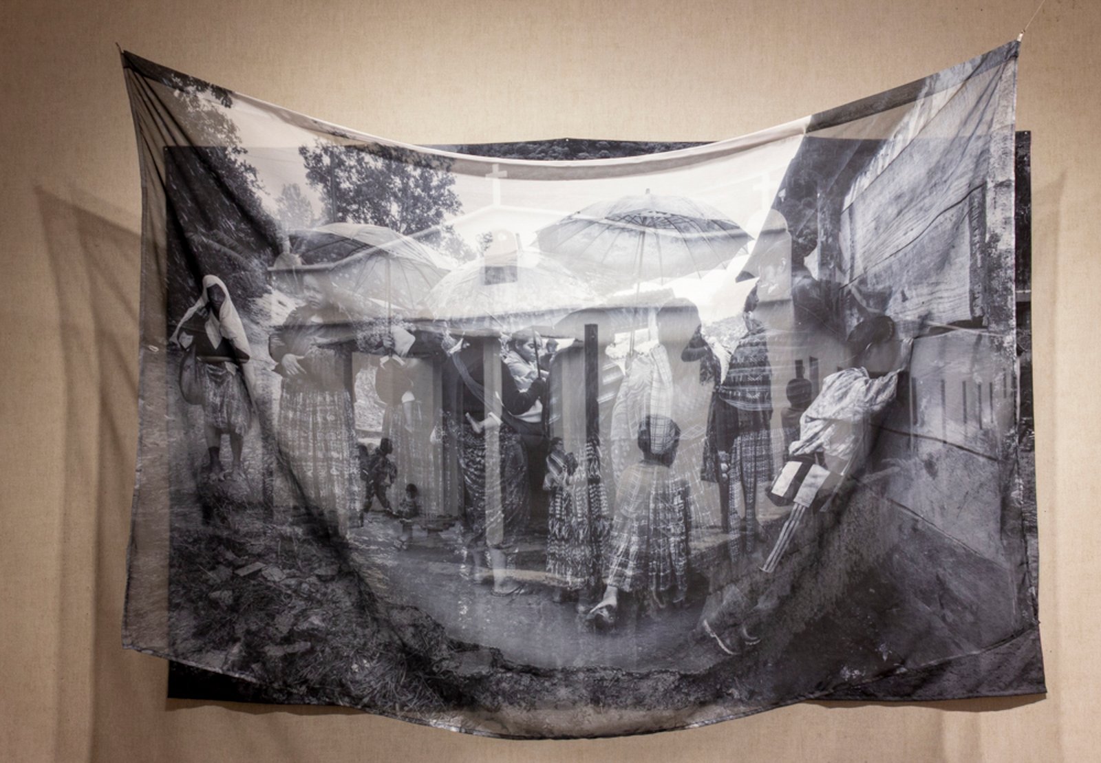 Two-layer sublimation installation — two distinct images on two polyester substrates: solid matte ground tacked to wall, sheer semi-transparent cloth hanging from ceiling — the images layer as a spatial double exposure